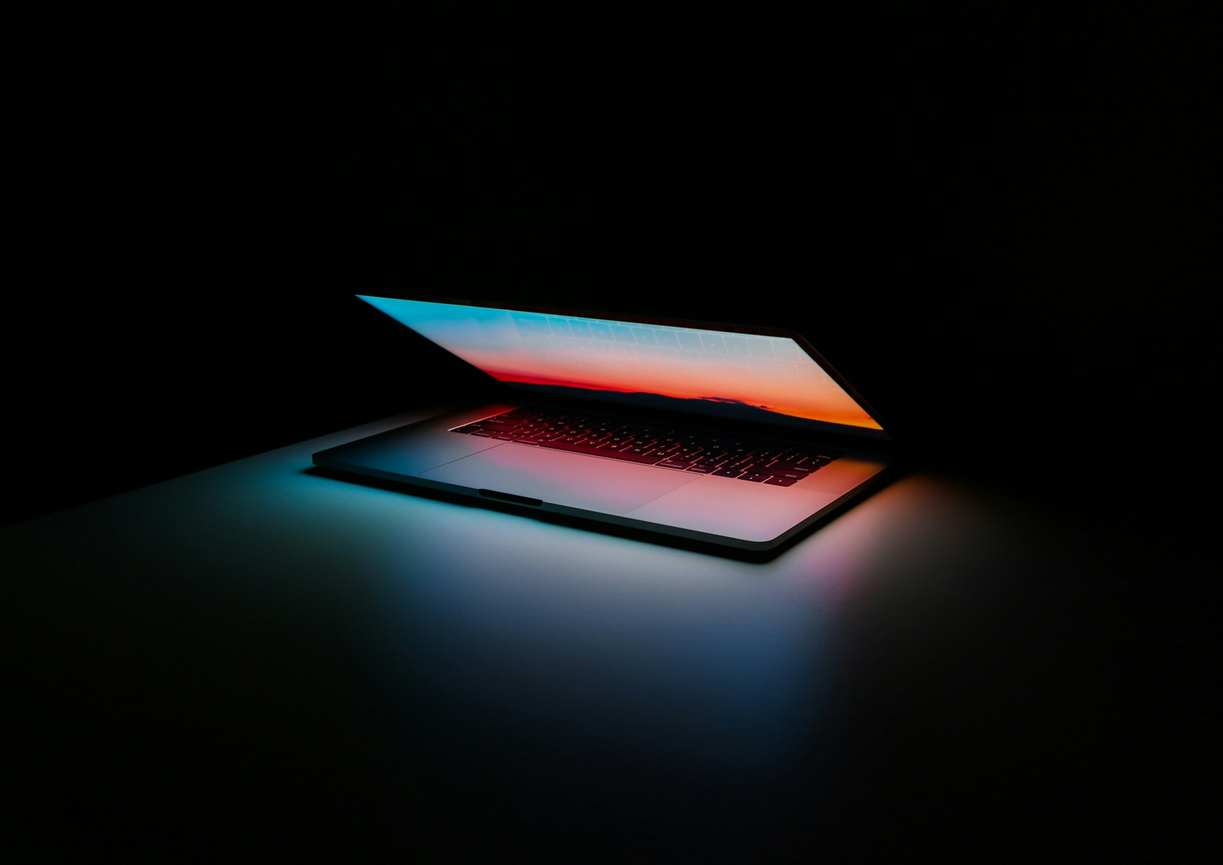Ordinateur portable entrouvert dans la pénombre, l'écran allumé diffusant une lumière colorée